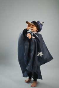 Young child looks to the sky through a homemade telescope while wearing a wizard cape and hat