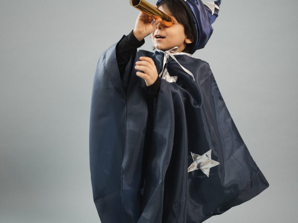 Young child looks to the sky through a homemade telescope while wearing a wizard cape and hat