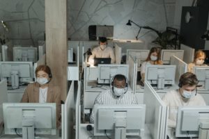 People wearing surgical masks sit at computers in a call center