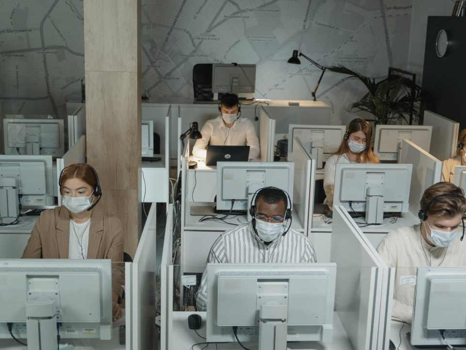 People wearing surgical masks sit at computers in a call center