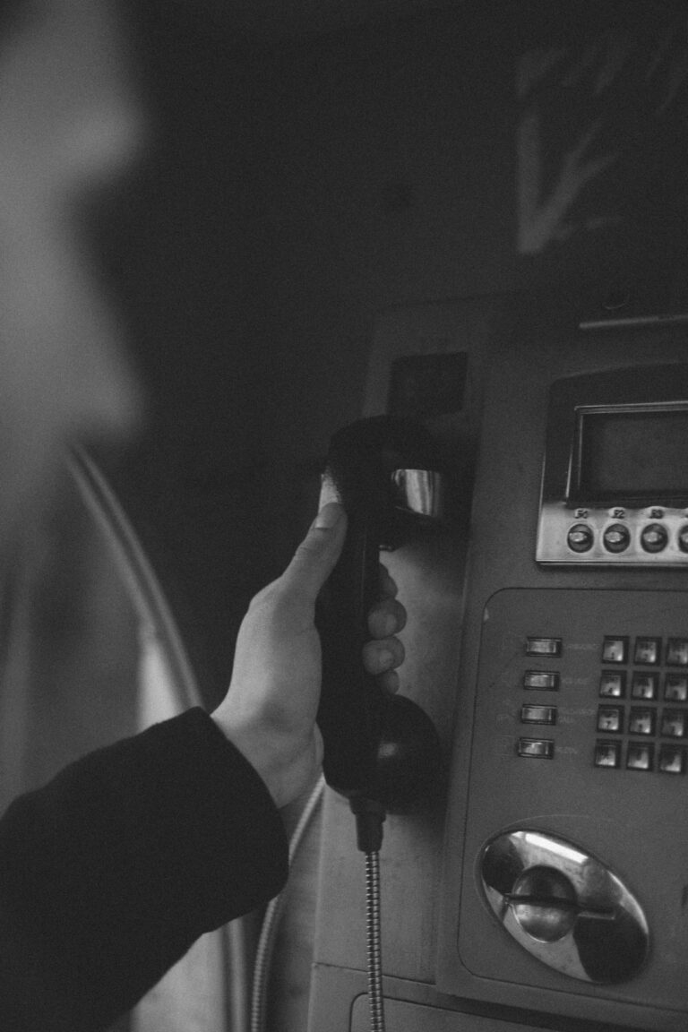 Black and white photo of a person's hand hanging up a payphone receiver.