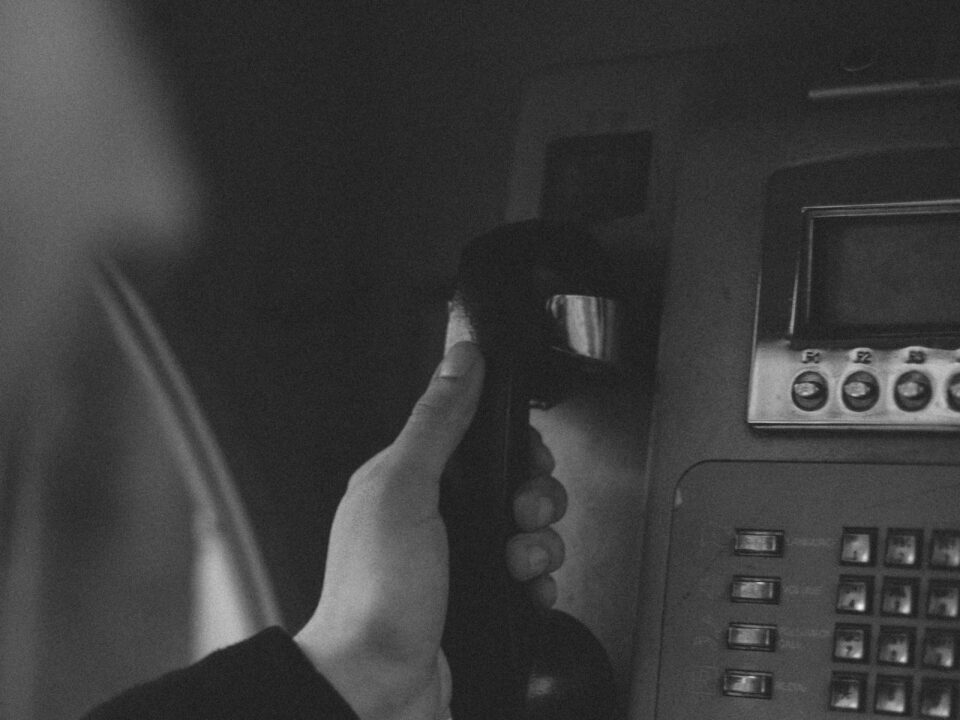 Black and white photo of a person's hand hanging up a payphone receiver.
